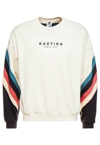 Off-white sweatshirt med KAOTIKO-logotyp och texten "Sedan 1999" på bröstet, med randiga ärmar i blått, svart, rött och krämfärg.