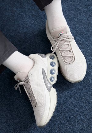 Light gray sneakers with mesh upper, round rubber accents, and visible air cushioning pods in the sole, paired with white socks.