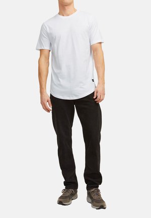 White cotton T-shirt with a round neckline, short sleeves, and a relaxed fit, paired with black corduroy pants and brown sneakers.