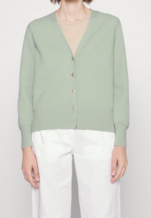 Cardigan côtelé vert clair avec un col en V, des manches longues et cinq boutons dorés. Porté sur un top beige et associé à un pantalon blanc.