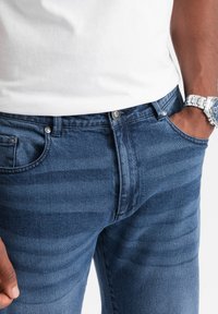 Jeans de mezclilla en un lavado azul oscuro con sutiles rayas horizontales, con cremallera, cinco bolsillos y acentos de metal.