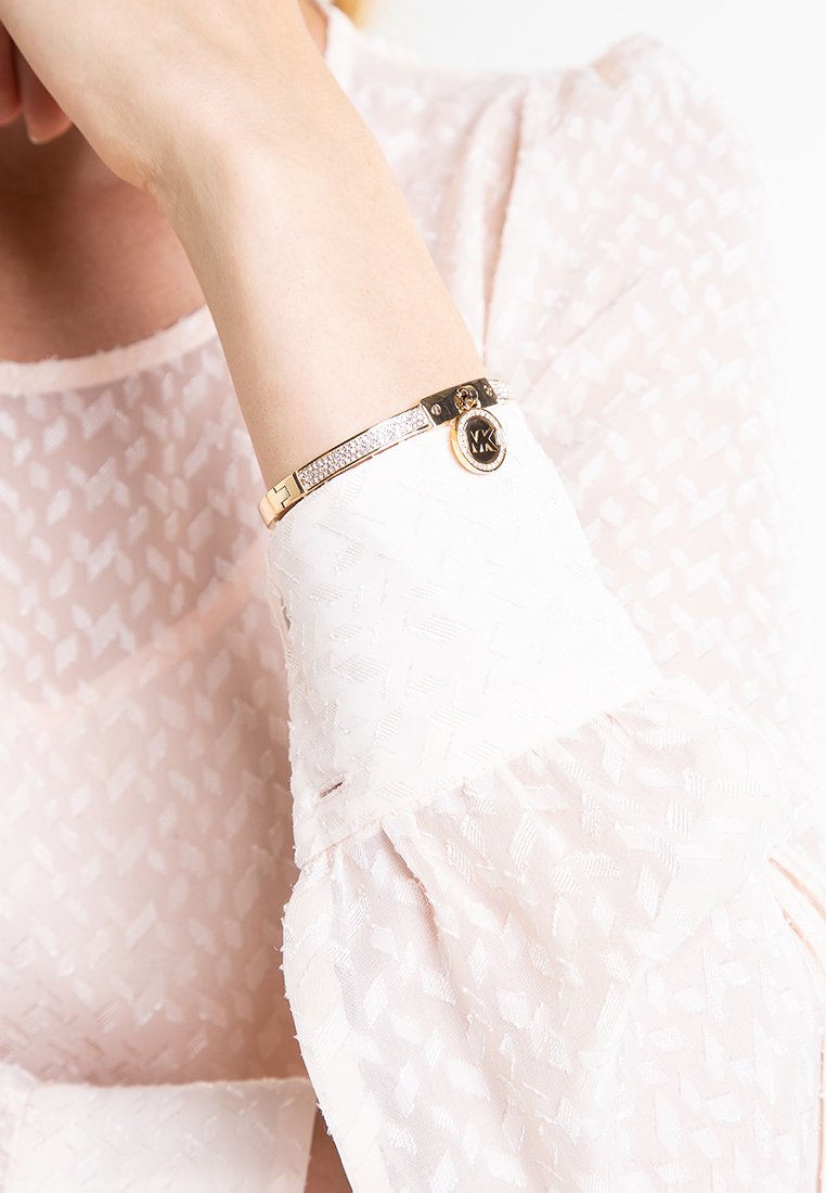 Bracelet doré avec un bracelet lisse, orné d'un rang de cristaux transparents et d'un charm circulaire comportant les initiales "MK."