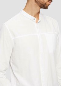 Witte linnen shirt met een mandarin kraag, knoopsluiting en een borstzak. Het heeft een ontspannen pasvorm en een lichte textuur in de stof.