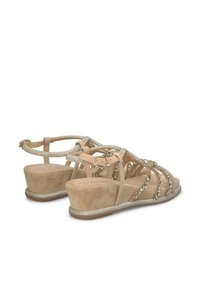 Beige Keilabsatzsandalen mit Schmuckakzenten, verziertem Kreuzriemen-Design und verstellbarem Knöchelverschluss. Weicher Wildledertextur mit metallischen Details.