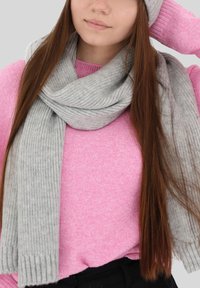 Sciarpa grigia lavorata a maglia drappeggiata attorno al collo sopra un maglione rosa, caratterizzata da una texture a coste e un design morbido e largo.