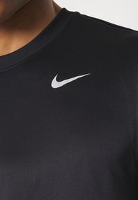 Czarna koszulka sportowa wykonana z gładkiego, elastycznego materiału. Posiada białe logo Nike w kształcie swooshu na górnej lewej stronie. Okrągły dekolt, dopasowany krój.