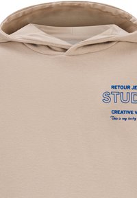 Beige hoodie van zacht materiaal met een grote blauwe print met de tekst "RETROUR JETE STUDIO CREATIVE V." en "Dit is mijn geluks."
