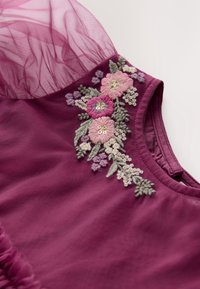 Robe violette avec manches bouffantes transparentes et motif floral brodé en rose, violet et vert autour du décolleté.