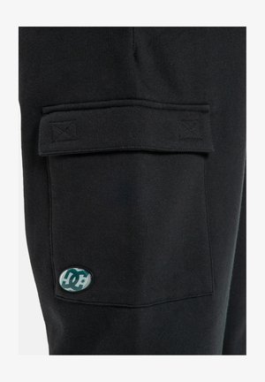 Zwarte cargobroek van zachte stof met een klepzak en een rond logopatch. Het ontwerp bevat gestikte details en heeft een relaxte pasvorm.