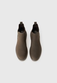 Zapatos marrones tipo slip-on con un acabado de ante suave, paneles laterales elásticos y una suela de goma baja para mayor flexibilidad y comodidad.