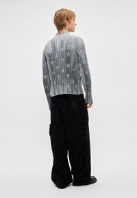 Γκρι ριγωτό πουλόβερ με αστέρια, συνδυασμένο με φαρδιά μαύρα παντελόνια κοτλέ, διακοσμημένα με σχέδιο κρανίου στην τσέπη.