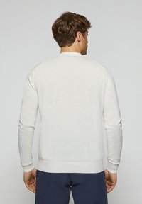 Maglione a maglia leggera color crema con maniche lunghe, collo rotondo e polsini a coste; texture liscia, design aderente e dettagli sottili al collo.