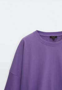 Felpa viola oversize con scollo rotondo, collo a costine e texture morbida. Etichetta visibile sul collo.