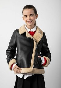 Czarna skórzana kurtka z beżowym kołnierzem i mankietami z owczej wełny, z zamkiem z przodu i dopasowanym krojem. Nosi się ją na białej koszuli i czerwonym swetrze.