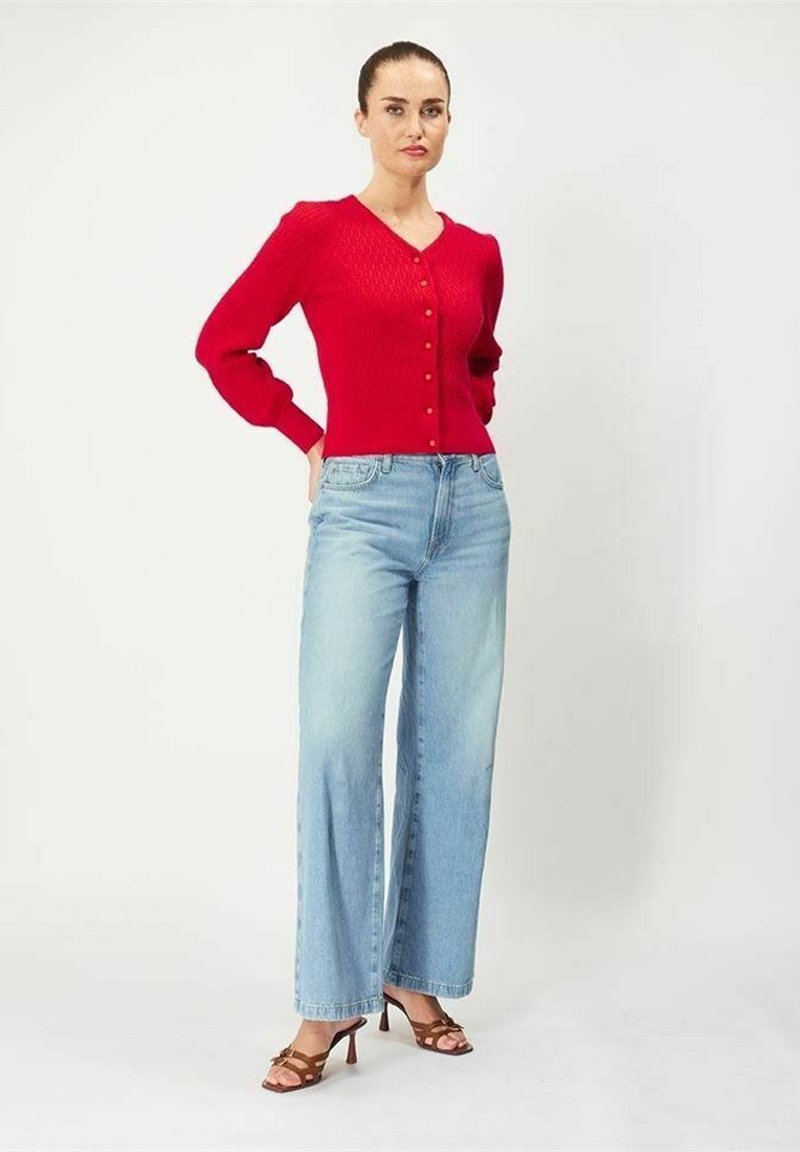 Röd stickad cardigan med V-ringning och knappstängning, kombinerad med ljusblå vida jeans. Bruna remsandaler fulländar outfiten.