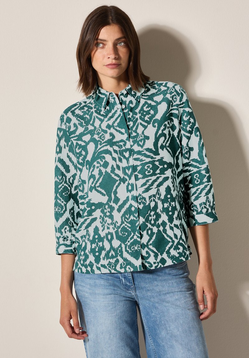 Camicia a fantasia verde e bianca con colletto, maniche lunghe e vestibilità comoda. Realizzata in un tessuto leggero con una texture liscia.