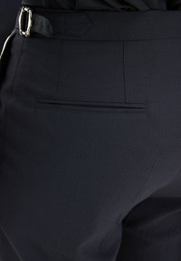 Pantaloni neri con una texture liscia, dotati di una tasca posteriore piatta e di un passante laterale per cintura con dettaglio della fibbia argentata.