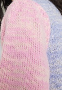 Pull en tricot avec un design en blocs de couleurs rose et bleu clair, fabriqué dans un tissu doux et texturé, présentant des motifs de couture distincts.