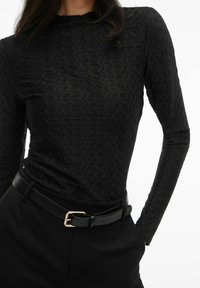 Musta pitkähihaista puseroa, jossa on tekstuuri; vartalonmyötäinen muotoilu. Yhdistetty korkeavyötäröisiin mustiin housuihin ja mustaan vyöhön, jossa on kultainen solki.