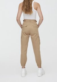 Pantalons cargo kaki à coupe décontractée, avec des poignets élastiques et des poches latérales. Le tissu semble léger et durable. Associés à des baskets blanches.