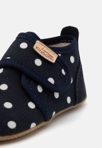 Tamsiai mėlynos spalvos audinio batai su baltais taškeliais, Velcro dirželiu ir smėlio spalvos logotipu; turi minkštą pamušalą ir lanksčią gumos padą.