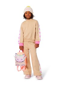 Set sportivo beige con accenti rosa; il sudore presenta maniche a fantasia. Zaino rosa con design di un gatto. Sneakers rosa chiaro.