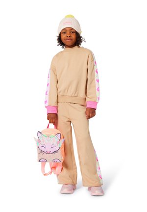 Beige sportoutfit met roze accenten; sweatshirt heeft gedessineerde mouwen. Roze rugzak met een kattenontwerp. Lichte roze sneakers.