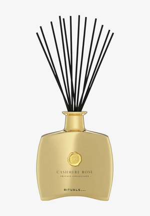 Goldfarbener Diffusor mit einem einzigartigen, teils geschwungenen Design. Verfügt über schwarze Ruten und ein Emblem-Detail auf der Vorderseite.