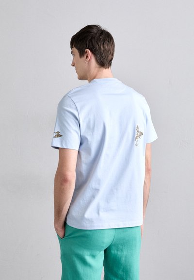Sublimt ljusblå bomulls-t-shirt med kort ärm, med ett tryckt mönster på ryggen och en liten detalj på vänster ärm.
