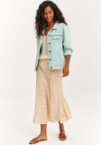 Svetlo modrá džínová bunda, krémový háčkovaný top, krémová sukňa s kvetinovým vzorom a hnedé ploché sandále. Mäkke textúry a voľný strih.