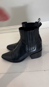 Fekete bőr bokacsizma hegyes orral, elasztikus oldalpanelekkel és texturált felülettel. Alacsony blokksarkú és hátul hurok fogantyúval.