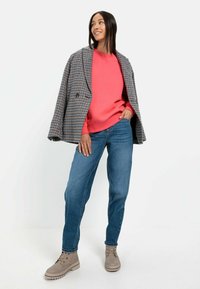 Kariertes, doppelt geknöpftes Blazer, leuchtend rosa Sweatshirt, blaue Jeans, beigefarbene Stiefeletten. Strukturierter Stoff, lässige Passform, Freizeitstil.