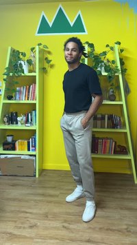 Light gray sweatpants with a drawstring, black fitted shirt, and white sneakers. Standing in front of green shelves and a yellow wall.