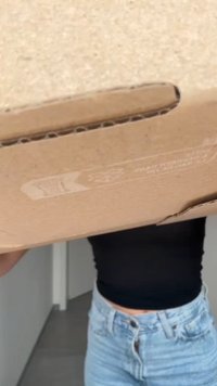 Brown cardboard box held from below, featuring a rectangular shape and visible packaging details. The background is blurred.