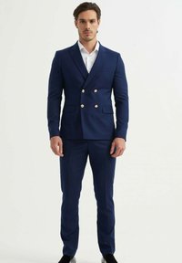 Costume bleu marine croisé avec des boutons dorés, coupe ajustée et texture lisse. Comprend un revers cranté et deux poches devant.