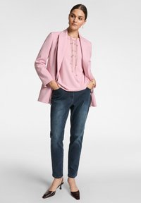 Ljusrosa blazer över en rosa topp, matchad med mörkblå jeans och bruna klackskor. Tillbehören inkluderar ett långt halsband med flera pärlor.
