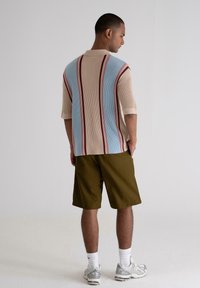 Knit polo shirt in cream, blue, and red vertical stripes; short sleeves and relaxed fit. Paired with olive shorts and athletic shoes.