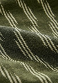 Tissu présentant une base verte avec des motifs linéaires blancs contrastants, mettant en valeur un tissage texturé et une profondeur subtile.