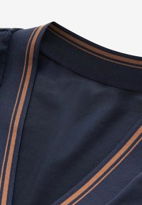 Indumento blu navy con colletto a costine e dettaglio a V, caratterizzato da strisce marroni parallele lungo i bordi.