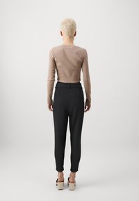 Světle hnědý dlouhý rukáv tričko v kombinaci s černými zúženými kalhotami. Kalhoty mají hladkou texturu a boční kapsy. Robustní béžové sandály.