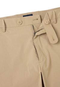 Beige katoenen broek met een rits- en knoopsluiting. Beschikt over een normale tailleband en zijzakken. Glad, lichtgewicht textuur.