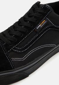 Svart sneaker laget av semsket skinn og slitesterk Cordura-stoff. Tykk svarte snørebånd, hvite sømmer og en teksturert gummisåle med detaljer.