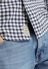 Niebiesko-biała koszula w kratę z guziczkami i metką; w połączeniu z dżinsami o teksturowanym materiale w jasnym odcieniu.