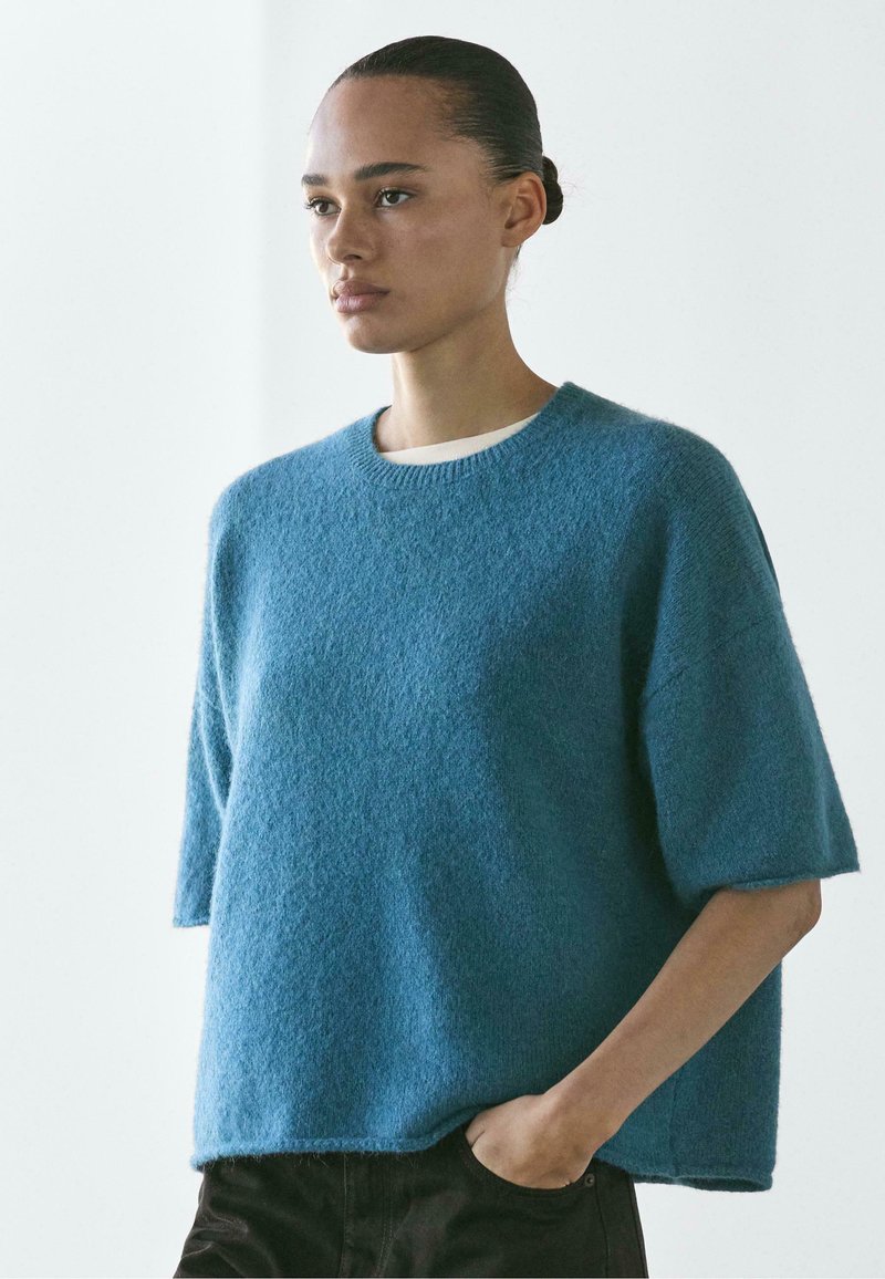 Maglione a maniche corte in tessuto morbido di colore azzurro chiaro con vestibilità comoda e scollo a coste, caratterizzato da un design minimalista.