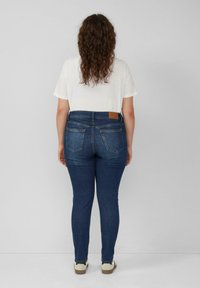 Donkerblauwe denim skinny jeans met een hoge taille, achterzakken en een tan leren label op de tailleband, gecombineerd met een wit t-shirt.