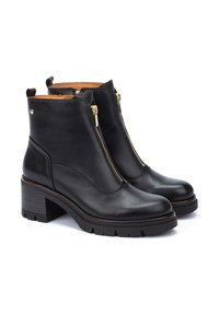 Botas de cuero negras hasta el tobillo con cremalleras doradas, tacón cuadrado y suela de goma texturizada. Presentan un acabado liso y un interior contrastante en tono marrón.