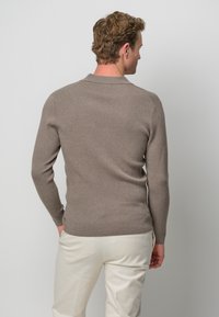 Brauner gerippter Pullover mit slim fit, langen Ärmeln und einer weichen Textur. Verfügt über einen klassischen Kragen und einen sauberen Saum, getragen über hellen Hosen.