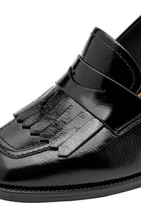 Mocassin en cuir noir brillant avec détail de franges et coutures cousues, montrant un gros plan sur le dessus avant et le côté de la chaussure.
