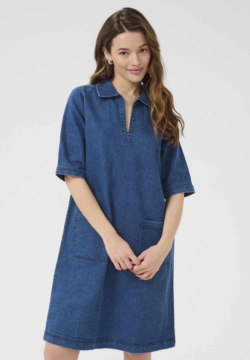 Denim jurk in diepblauw met korte mouwen, kraagloos ontwerp, twee voorzakken en zichtbare stikdetails. Zachte stoftextuur.