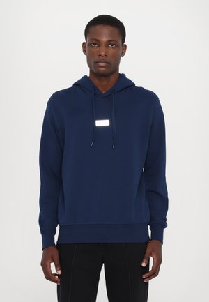 Mörkblå hoodie i mjukt tyg, med en framficka i kengurustil och dragsko, samt en rektangulär logotyp på bröstet.